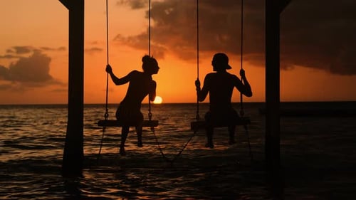 Romantic Couple Sitting on Swings at Tropical Sunset