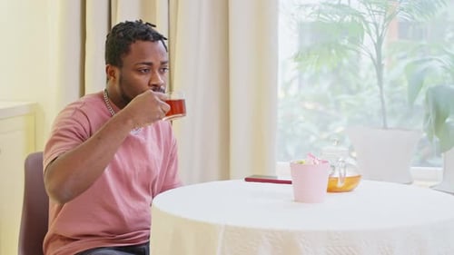 Guy Hipster afro-américain buvant une tisane assis dans la cuisine à la maison