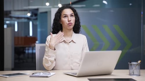 Businesswoman is hot while working on a laptop sitting at workplace in office. Female employee waves