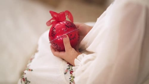 slow motion shot Over the shoulder of kid in a Christmas white dress holding a red bauble - close up