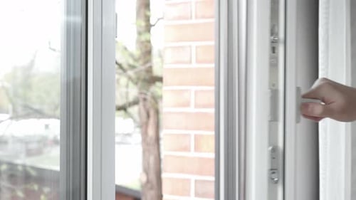 The man closes the PVC plastic window and turns the handle on the window frame.