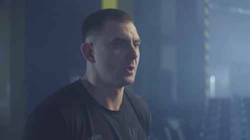 Caucasian Man Picks Up Dumbbells and Starts Swinging His Arms in the Gym