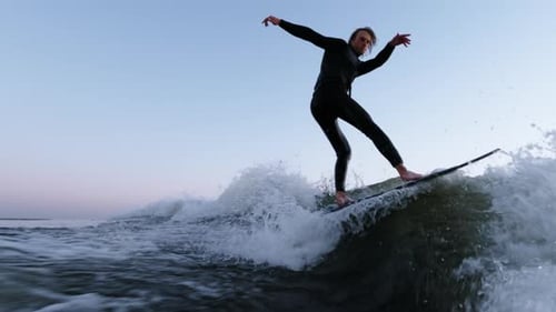 A Skilled Surfer Maneuvers Through Dynamic Waves at Dusk Showcasing Balance and Control While
