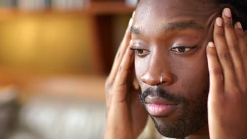 African American man feeling tension, pressing temples and rubbing forehead on couch, nose ring