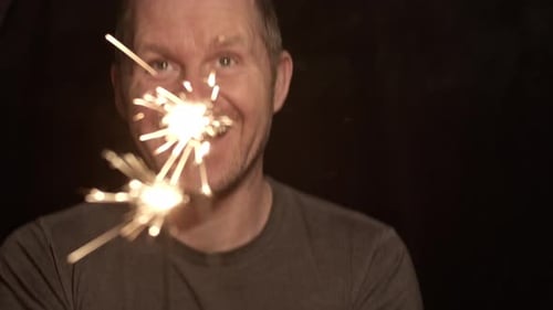 Man Smiling and Holding Sparklers on Black Background