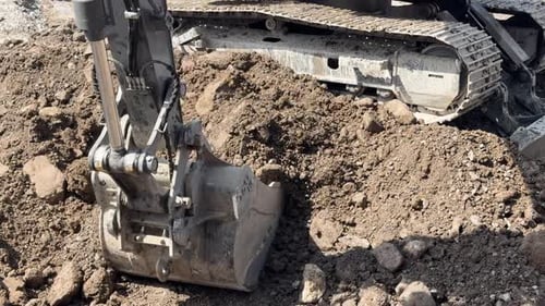 Front loader tractor scoops dirt and rocks on construction site, lifting and dumping off-camera into
