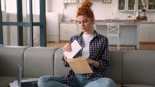 Serious Woman Opens Letter on Living Room Couch