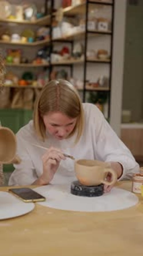 Potier concentré finalisant le design de la tasse en céramique avec une peinture détaillée dans un style organisé et lumineux