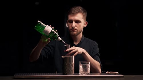 Male Bartender Hands Holding Bottle and Masterfully Pours Beverage Into Steel Jigger on a Black