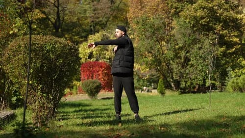 A Young Sportsman is Doing Warmup in the Autumn Park