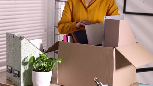 Despido. Mujer empacando sus objetos personales en una caja de cartón en la mesa de la oficina, primer plano