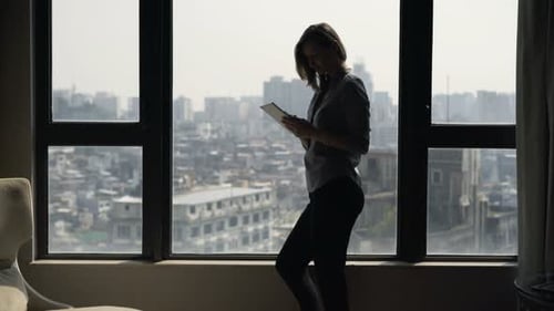Woman Uses Tablet Device Next to Large Window