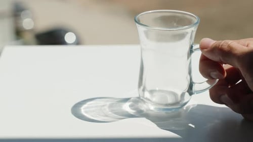 Ich stelle eine leere Tasse auf den Tisch und gieße heißen Tee hinein. Sommer, Schatten auf dem Tisch. Nahaufnahme
.