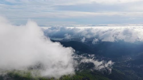 Vista aérea de vastas montañas verdes cubiertas de niebla y nubes con un cielo despejado de fondo