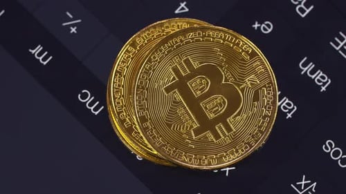 Goldene Bitcoins liegen auf einem Taschenrechner, der in einem Smartphone eingeschaltet ist