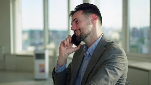 Young Adult Man Smiles and Talks on Phone at Desk