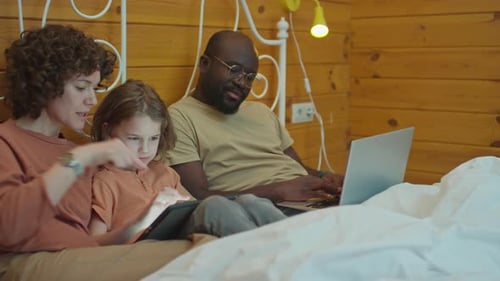 Family Relaxing in Bed With Technology