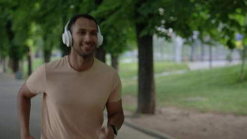 Smilled Afro American Man is Running in the Park Area Wearing Headphones