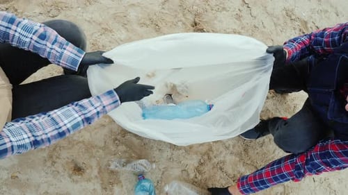 Los voluntarios ponen basura plástica en una bolsa para limpiar la playa y cuidar el medio ambiente | Vista desde arriba