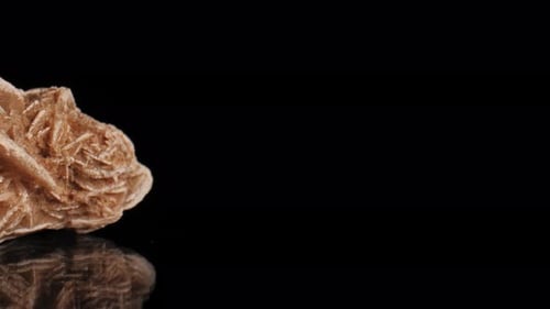 Smooth captivating pan of desert rose crystal selenite lit against a black background. Cinematic mac