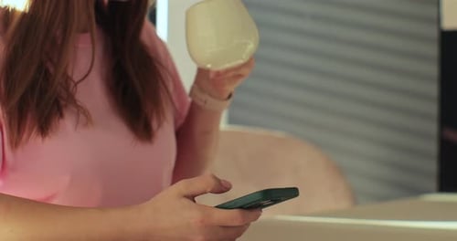 Woman Using Smartphone and Drinking From Cup