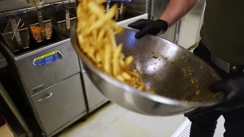Restaurant Chef Seasoning and Tossing French Fries in Bowl