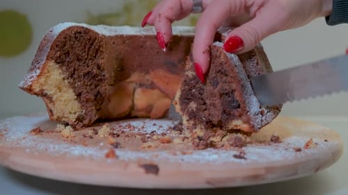 Traditional marble cake on wooden plate, femal hands cutting cake into slices