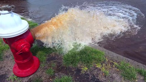 Eine Tiefwinkelaufnahme eines rot-weißen Hydranten, der an einem sonnigen Tag rostiges Wasser auf die Straße sprüht
