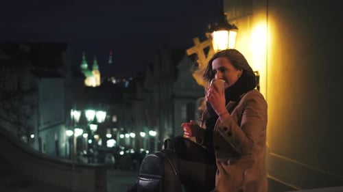 Young woman using mobile phone outside at night, Prague sights in background, Czech Republic