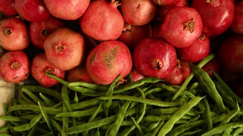 Vendor Arranging Pomegranates and Green Beans on Market Stall