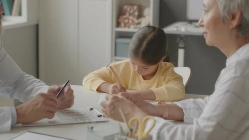 Young Girl Writes at Doctor's Office with Family