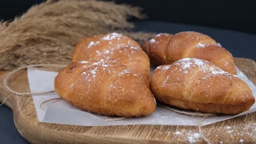 Golden Croissants with Powdered Sugar on Wood Board