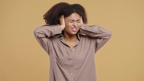 Irritated Young African Woman Covering Ears Ignoring On Beige Noise Shouts