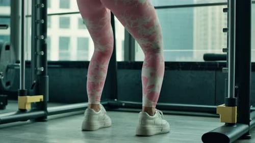 Mujer asiática fuerte y en forma haciendo sentadillas profundas en Smith en el gimnasio, vista de ángulo bajo