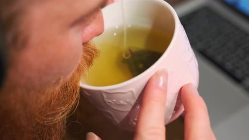 Close-up, redbearded man wearing headphones drinking green tea in a ceramic mug