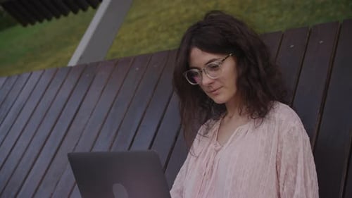 Handheld Close Up of a Curly Caucasian Woman Working on Her Laptop Computer on a Park Bench