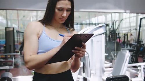 Fitness Trainer Documenting Workout Plan in Modern Gym During Afternoon Session