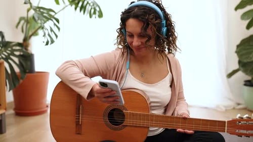 Woman with Guitar Listens to Music in Apartment