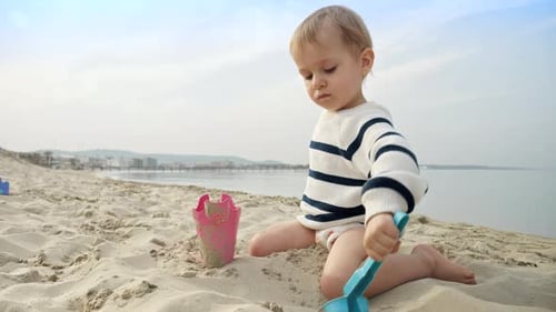 Happy baby boy playing with a shovel on the sandy beach during a summer vacation