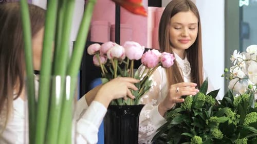 Deux ouvrières, fleuristes, debout à une table dans un atelier de fleurs, tenant un bouquet de fleurs et