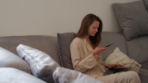 Young Woman Uses Laptop and Smartphone on Sofa