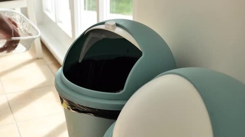 Hand Throwing Waste into a Blue Trash Can