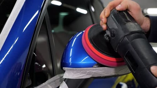 A Man Polishes a Blue Car with a Car Polishing Machine at a Car Dealership