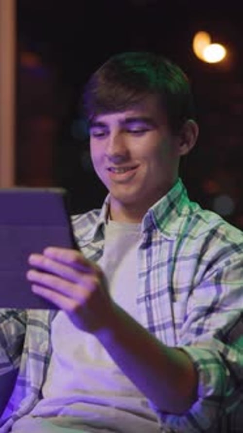 A Young Man Lounges in a Dim Room Absorbed in His Devices