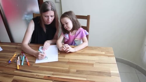 Mutter hilft Tochter beim Zeichnen mit Markern auf Papier zu Hause
