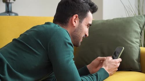 Man Relaxing on Couch While Using Cellphone