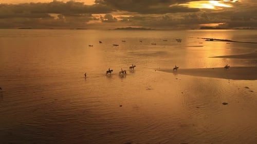 Golden Beach Sunset with People Riding Horses Through Shallow Sea at Low Tide Creates Dramatic