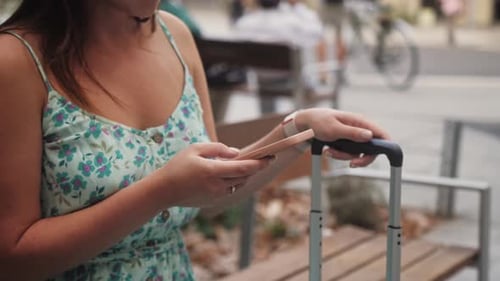 Woman with Smartphone and Luggage Sits on Bench
