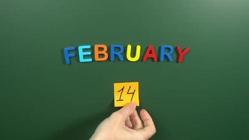 Hand sticking a sticker 14 February calendar day on school board. 14 date of February. Fourteenth