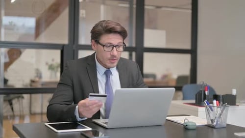 Man Looking At Laptop With Credit Card In Hand